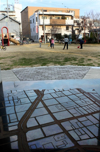 震災の悲惨さを伝える慰霊碑（手前）。町並みはすっかり変わった＝神戸市長田区御蔵通５、御蔵北公園