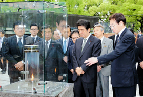 久元喜造・神戸市長（右端）から「１・１７希望の灯り」について説明を受ける安倍晋三首相＝１６日午前、神戸市中央区の東遊園地（代表撮影）