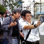 阪神・淡路大震災当時の被害を端末で確認しながらまちを歩く参加者＝神戸市兵庫区松本通