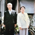 金婚式の式典に出席するため、正装に身を包む芝重吉さん（左）とヒデ子さん。右側の建物が阪神・淡路大震災で崩壊した自宅の文化住宅＝１９９１年４月、神戸市中央区筒井町３（家族提供）