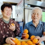 愛媛県の友人から届いたミカンを手に取る深田勲さん（右）と洋子さん＝神戸市東灘区本山南町８
