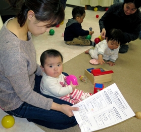 防災グッズチェックリストを手にする母親と、遊ぶ子どもら＝小久保１