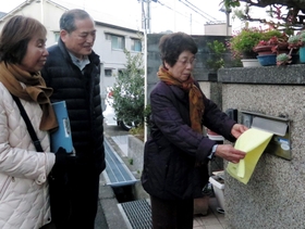 郵便受けにタオルを掛ける女性（右）と、見守る民生委員ら＝明石市太寺４
