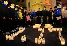 「２２」「１・１７」の文字をかたどったろうそくを囲み、黙祷をささげる住民ら＝淡路市郡家