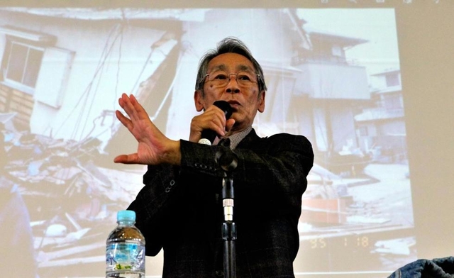 全壊した自宅の写真を背に生徒らに語り掛ける田村勝太郎さん＝小野中