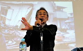 全壊した自宅の写真を背に生徒らに語り掛ける田村勝太郎さん＝小野中