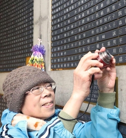 父の名前が刻まれた銘板にカメラを向ける本美穂子さん＝東遊園地（撮影・大森　武）