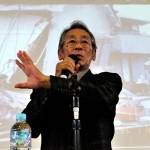 全壊した自宅の写真を背に生徒らに語り掛ける田村勝太郎さん＝小野中