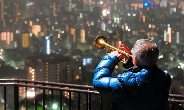 雨の中、神戸の街へ思いを込めて演奏するトランペット奏者松平晃さん（７６）＝２０１８年１月１７日、神戸市中央区神戸港地方、ビーナスブリッジ（撮影・田中靖浩）