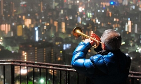 雨の中、神戸の街へ思いを込めて演奏するトランペット奏者松平晃さん（７６）＝２０１８年１月１７日、神戸市中央区神戸港地方、ビーナスブリッジ（撮影・田中靖浩）