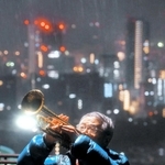 雨の中、神戸への思いを込めて演奏する、川崎市のトランペット奏者松平晃さん（７６）。「来られる限りは神戸に来て演奏したい」＝１７日午前６時２２分、神戸市中央区諏訪山町、ビーナスブリッジ（撮影・田中靖浩）