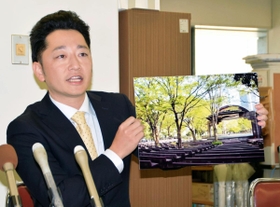 「１・１７のつどい」東京会場の詳細について、日比谷公園の写真パネルを示しながら話す藤本真一委員長＝１８日午前、神戸市役所