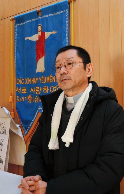 「顔見知りの関係をつくることが大切」と語る神田裕さん。聖堂の壁には、ベトナム、ハングル、日本語で表記されたタペストリーがある＝カトリックたかとり教会