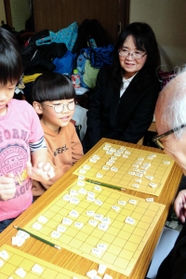 隆文さんの師匠森信雄さんが営む宝塚市の将棋教室で、子どもらを見守る船越明美さん（奥）＝宝塚市清荒神１