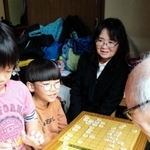 隆文さんの師匠森信雄さんが営む宝塚市の将棋教室で、子どもらを見守る船越明美さん（奥）＝宝塚市清荒神１