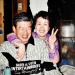 照れながら妻の久代さんと写真に納まる加久幾康さん（左）