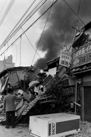 損壊した建物の２階部分から家財を運び出す住民。自販機が横倒しになっている＝１７日午前、神戸市長田区大道通３
