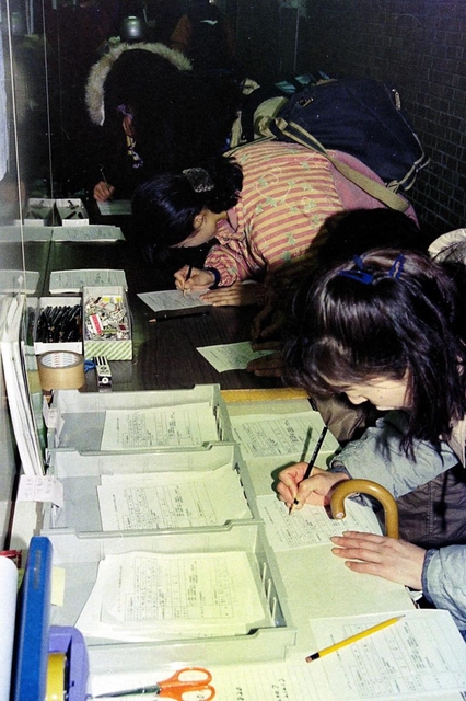西宮市役所でボランティアの受付窓口で書類を記入する人々＝２２日午後、西宮市六湛寺町