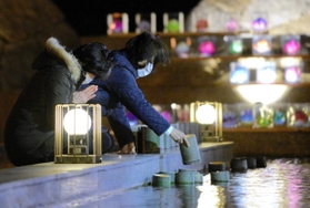 犠牲者を悼み、明かりのともる竹筒を水に浮かべる人たち＝１７日午前５時２６分、淡路市小倉、北淡震災記念公園（撮影・田中靖浩）