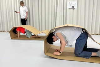 輪っか状の段ボールを使い、低い姿勢での避難を体験する参加者ら＝中央区文化センター