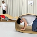 輪っか状の段ボールを使い、低い姿勢での避難を体験する参加者ら＝中央区文化センター