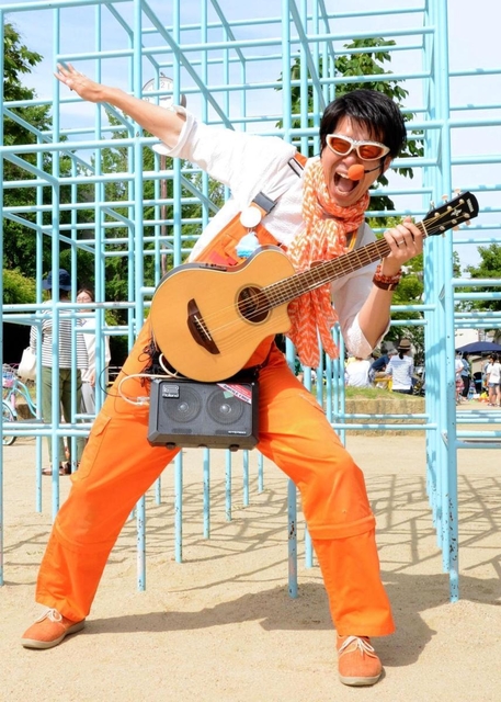 オレンジの衣装にギター片手でダンスや歌を披露する「須磨のスター」しんごお兄さん＝須磨区南町１、稲葉公園
